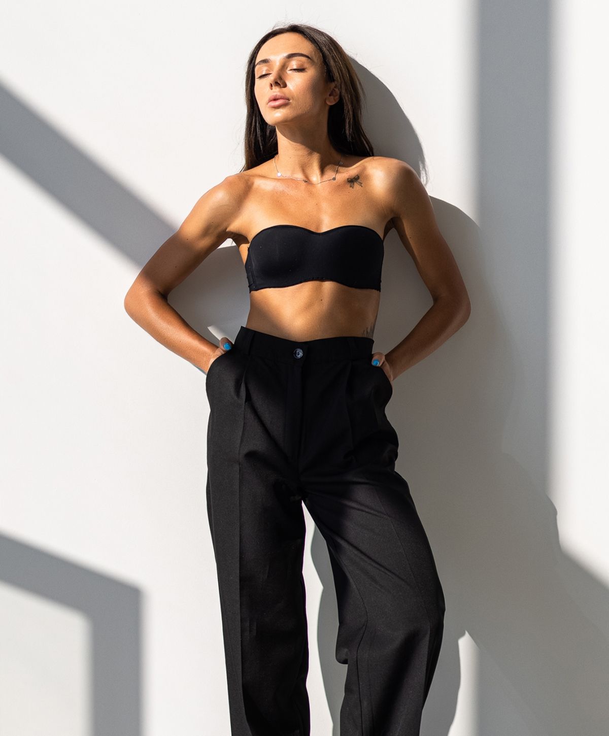 Model posing against a wall in stylish attire.