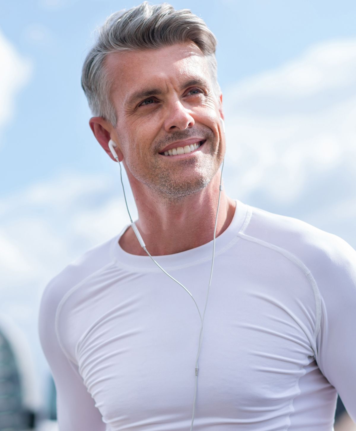 Smiling man in sportswear with earbuds outdoors.
