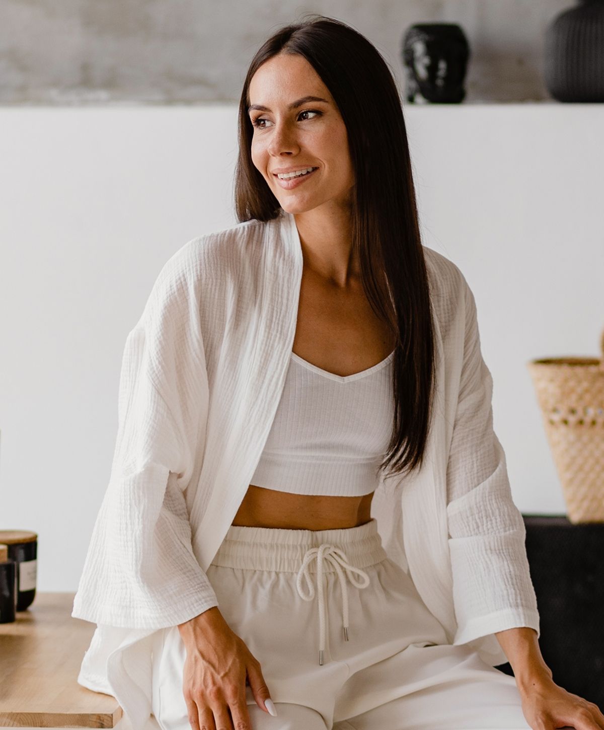 Woman in white outfit sitting indoors, smiling.