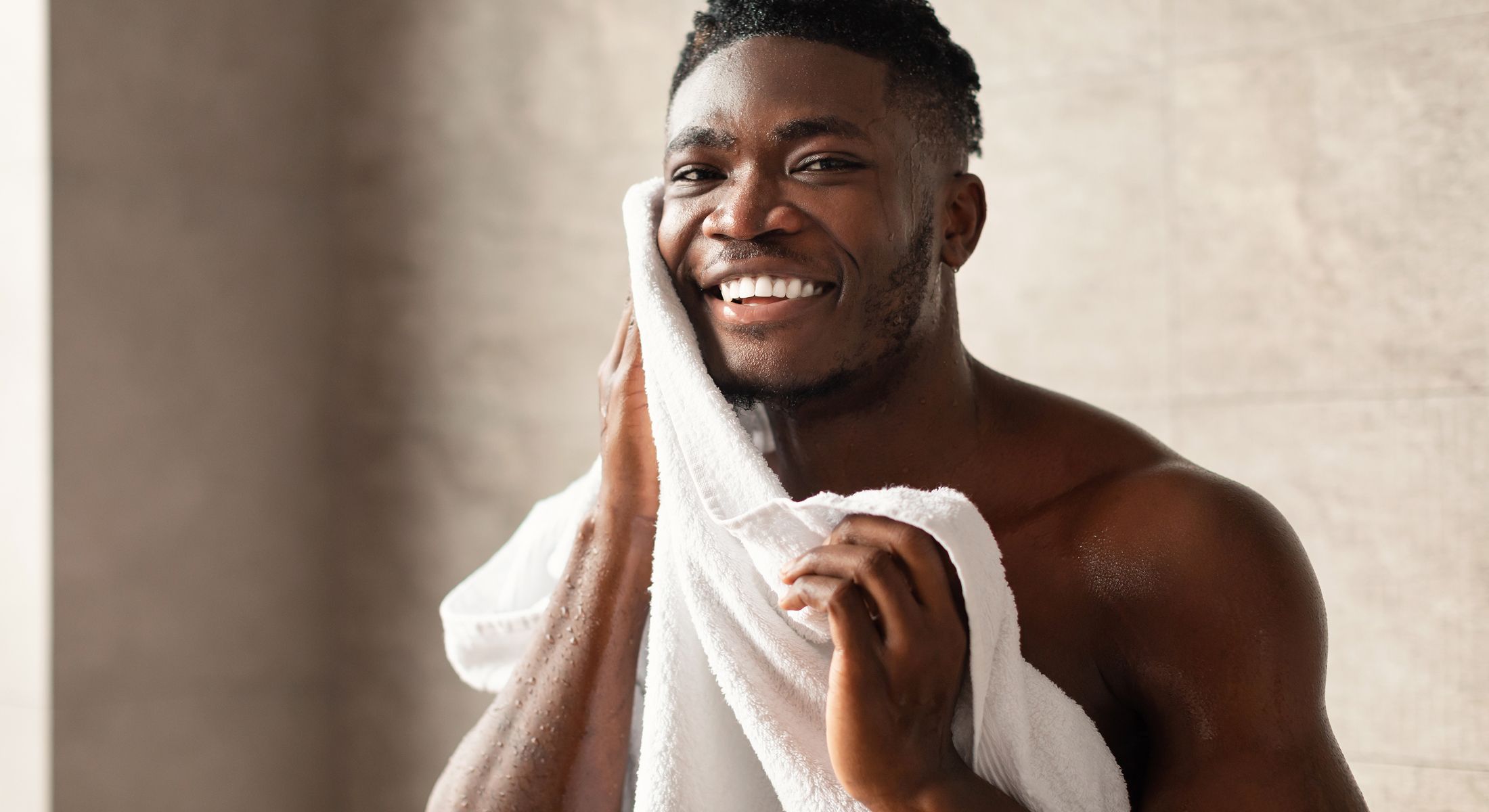 Smiling man drying face with towel in shower.