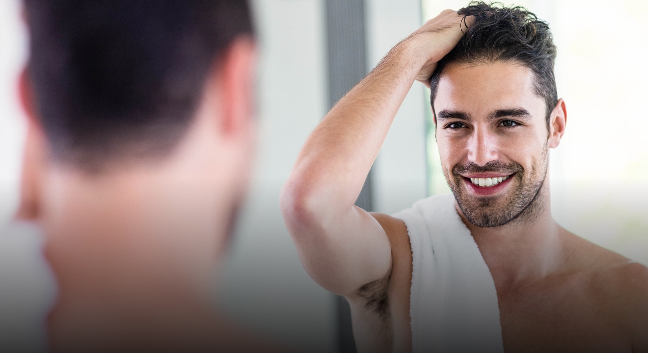 Smiling man grooming himself in front of mirror.